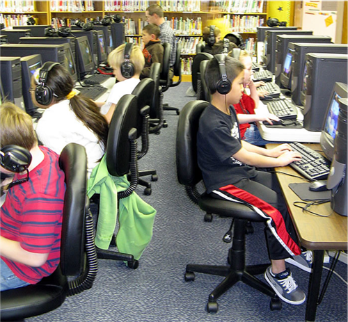 students sitting at computers with headphones in computer lab